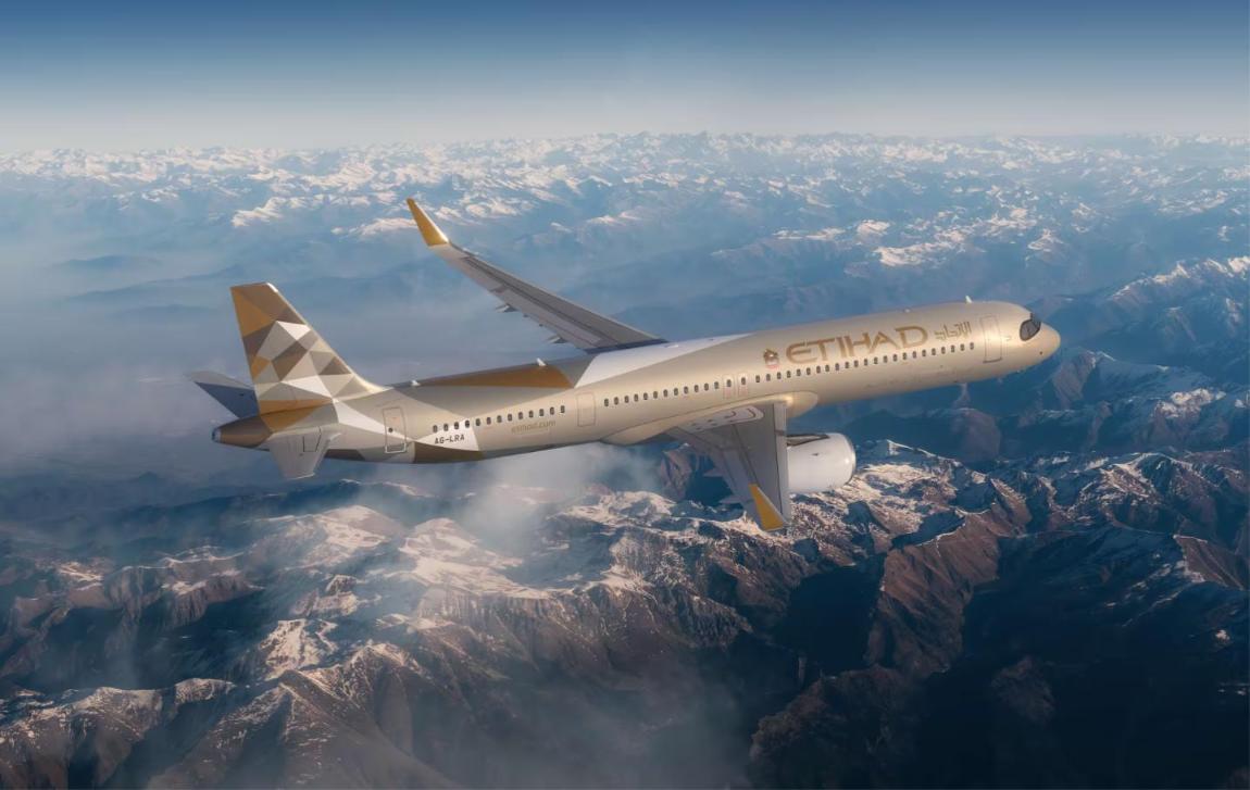 Etihad Airways Airbus A321LR in gold and white livery flying over snow-covered mountains