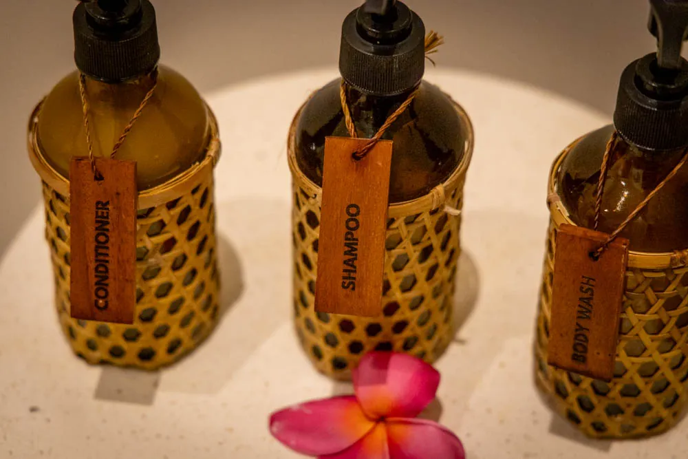 Shampoo, conditioner and body wash bottles in woven rattan sleeves with a frangipani flower