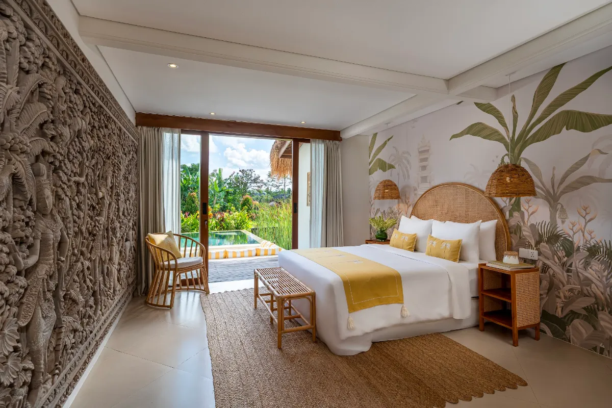 Gaia bedroom at Goddess Retreat Ubud with carved stone wall, rattan headboard and doors opening onto the pool and rice fields