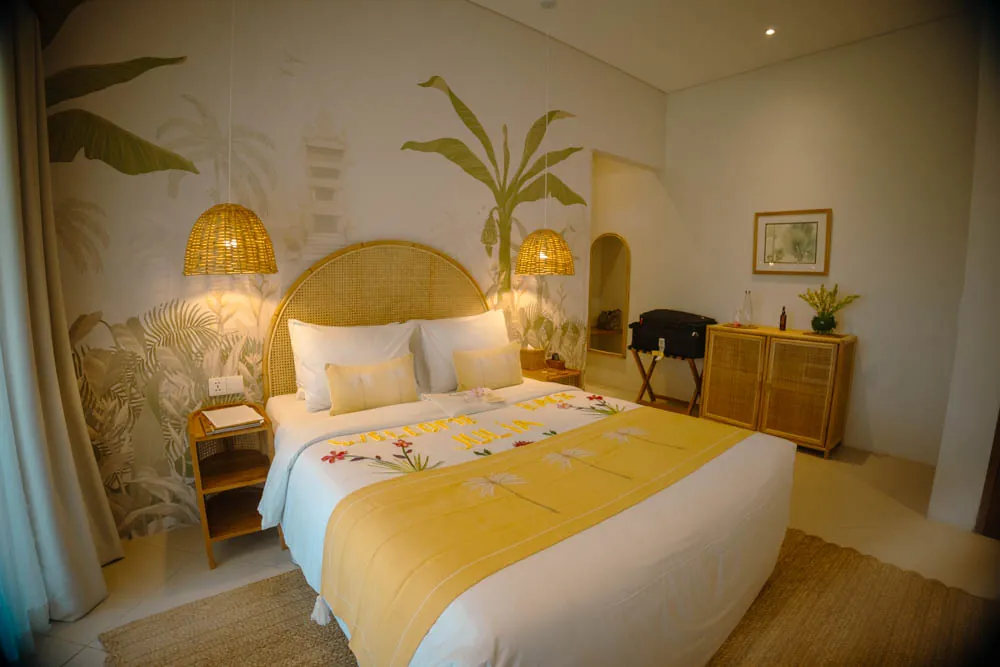Gaia room bedroom at Goddess Retreat Ubud with rattan headboard, yellow bed runner and tropical mural