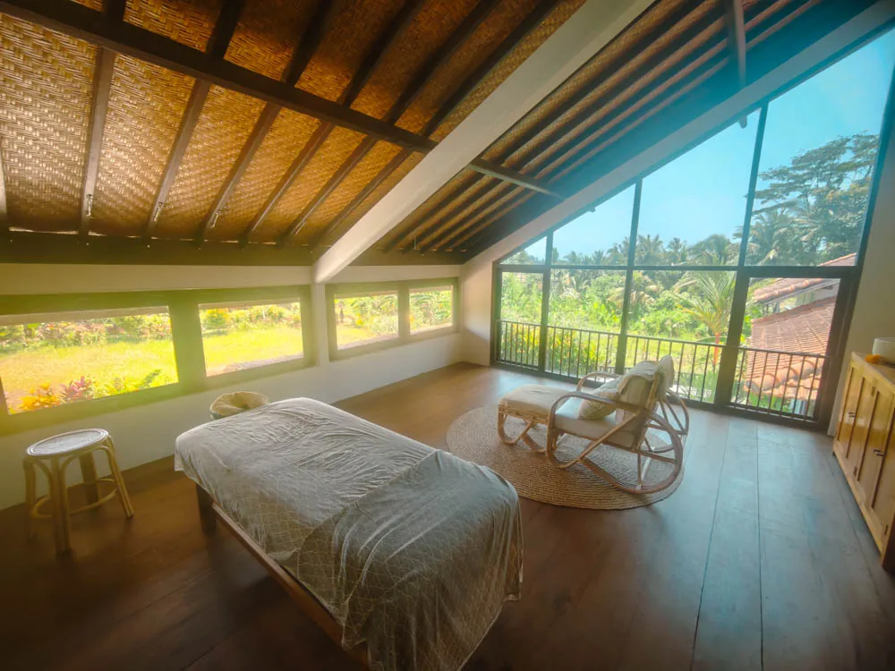 Spa treatment room with massage table and floor-to-ceiling windows over the rice fields at Goddess Retreat Ubud