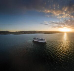 Rendering of Oceania Aurelia at anchor off a coastline at sunset