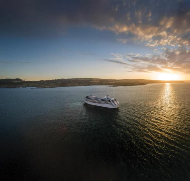 Rendering of Oceania Aurelia at anchor off a coastline at sunset