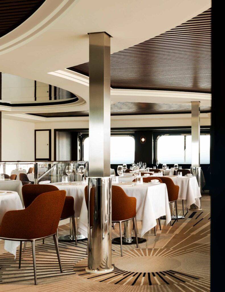 La Terrasse restaurant on Orient Express Corinthian, with white-clothed round tables, curved chairs and a wall of windows