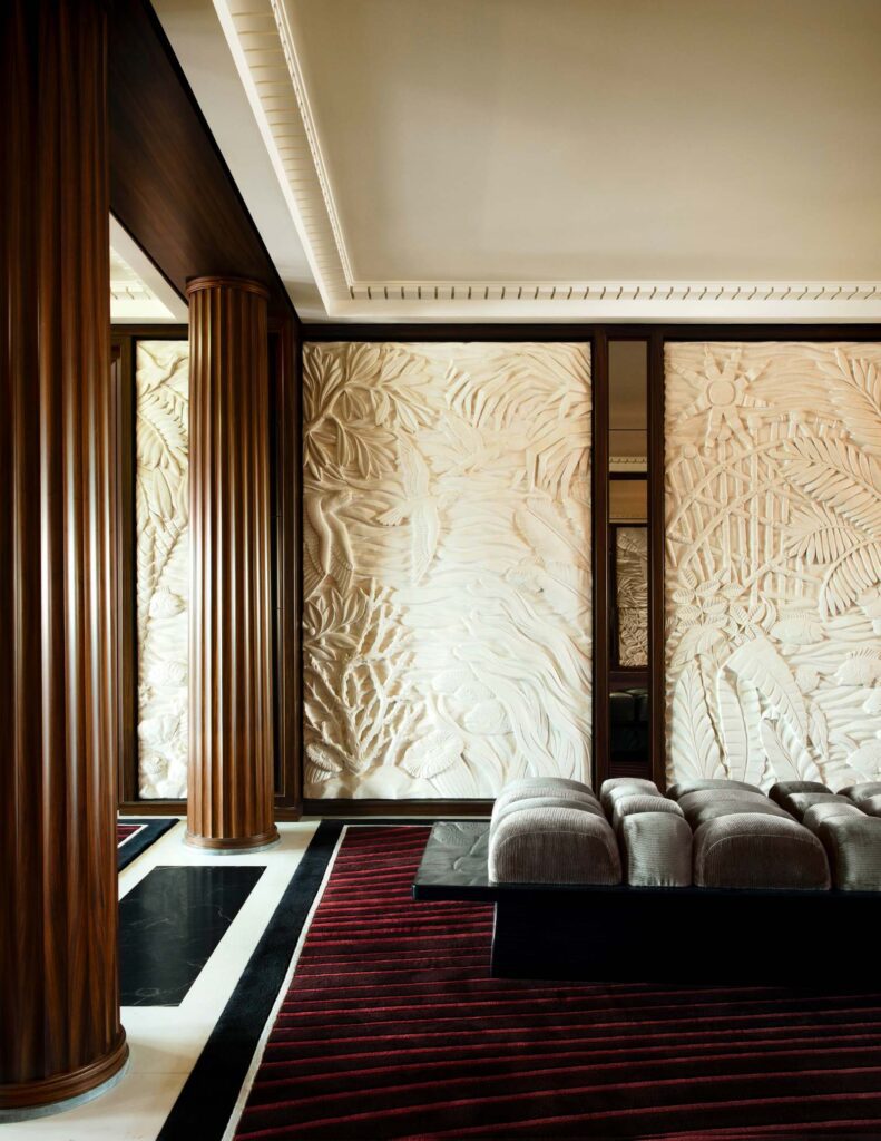 The reception on Orient Express Corinthian, with sculpted cream wall panels, a low bench and a patterned carpet