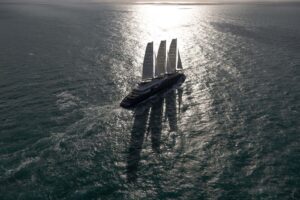 Aerial view of Orient Express Corinthian under its three rigid sails on open sea, with sunlight on the water