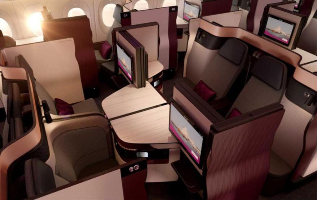 Qatar Airways Qsuite business class with four centre seats opened into a quad around a shared table, burgundy and cream finishes