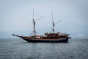 Scubaspa Zen two-masted phinisi at anchor under a hazy sky, October 2026