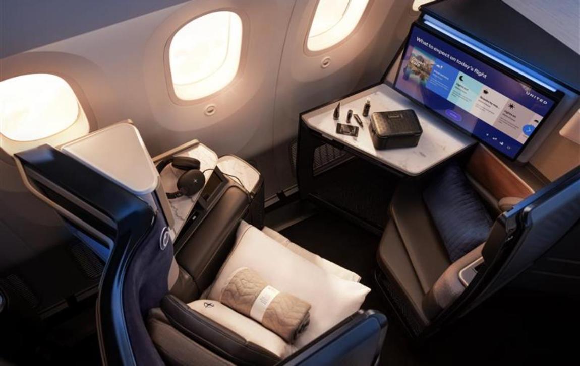 United Polaris Studio suite on the 787-9 with a 27-inch screen, marble-effect side table, companion ottoman, bedding and amenity kit laid out